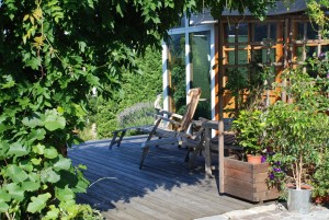 Sitzplatz eingerahmt von Topfpflanzen und Kletterpflanzen an der Gartenhütte, Holzterrasse